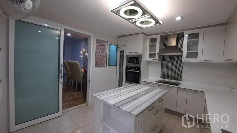 Townhouse for rent or sale in Suan Luang, Bangkok - Modern white kitchen with island, built-in oven, and range hood.