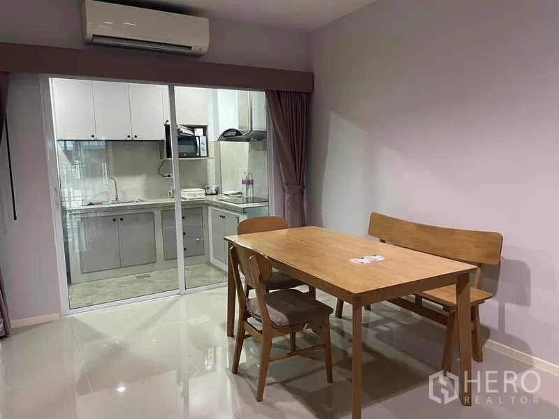Townhouse for rent in Suan Luang, Bangkok - Dining area with wooden table set facing a sliding glass door to the kitchen.