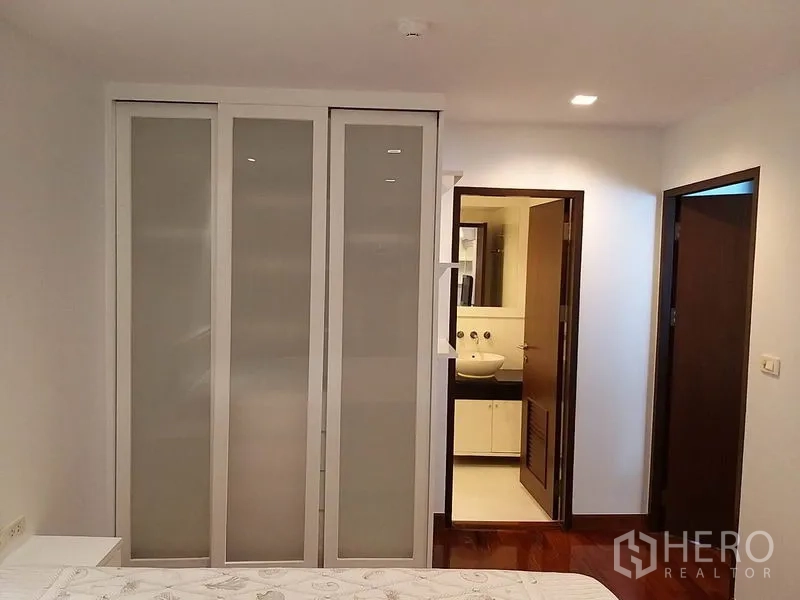 Condominium for rent or sale in Pathum Wan, Bangkok - Bedroom with frosted sliding-door wardrobe and entry to a modern bathroom.
