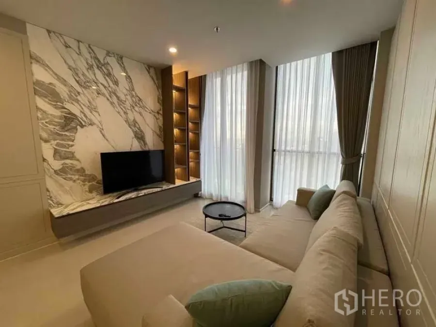 คอนโด ให้เช่าในPathum Wan, Bangkok - ห้องนั่งเล่นโซฟาเข้ามุม ผนังทีวีลายหินอ่อน และหน้าต่างเต็มผนัง