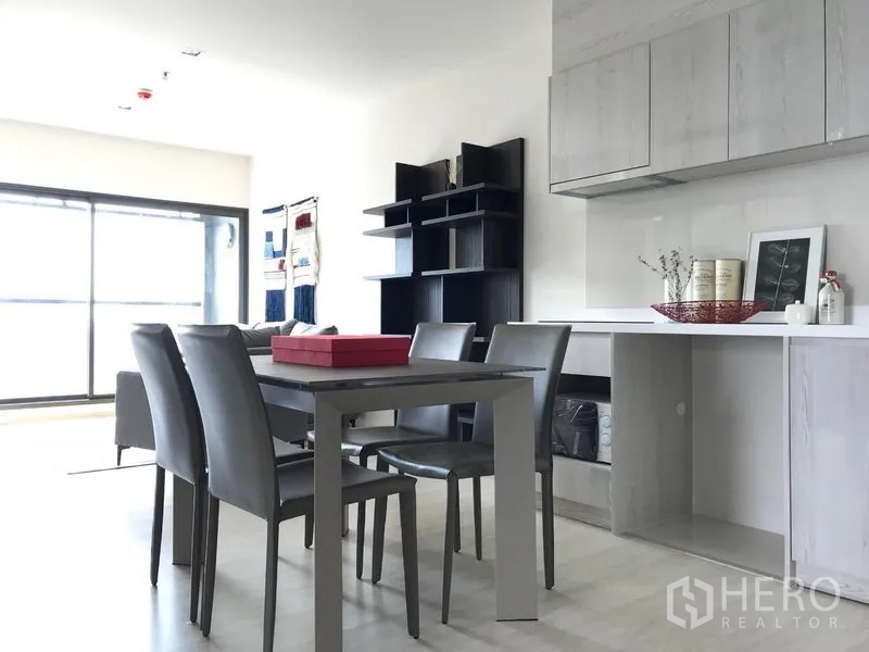 Condominium for rent in Khlong Toei, Bangkok - Open-plan dining space and light wood kitchen with shelving facing floor-to-ceiling windows.