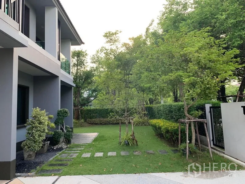 Detached House for rent or sale in Bang Phli, Samut Prakan - Side yard with stepping stones, mature trees and the shaded house facade.