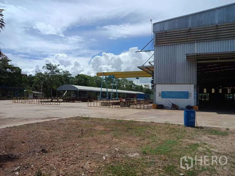 Factory for sale in Chachoengsao - Concrete loading yard with covered work areas beside the metal-clad factory building.