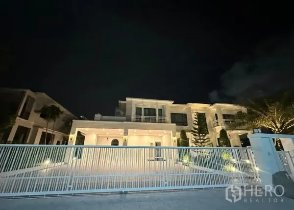 独立式住宅 出租在Bang Phli, Samut Prakan - 夜景下透过白色金属栅栏看到灯光辉映的现代住宅。