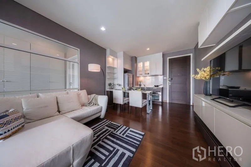 Condominium for rent or sale in Watthana, Bangkok - Stylish open-plan lounge with sofa, rug, dining set and kitchen cabinetry.