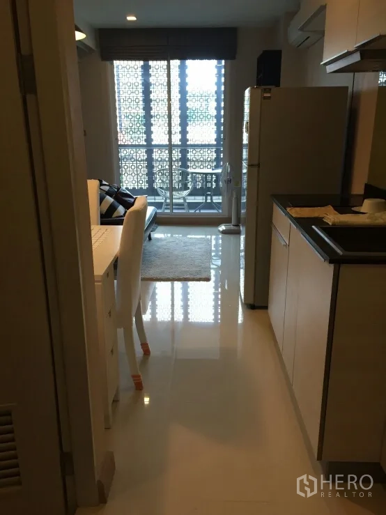 公寓 出租在Watthana, Bangkok - 从厨房望向客厅与阳台，阳台有花纹遮挡与小圆桌椅，开放式布局。