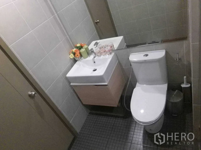 公寓 出租在Bang Na, Bangkok - 现代风浴室，灰色瓷砖、独立洗手台、宽幅镜面与坐便器。