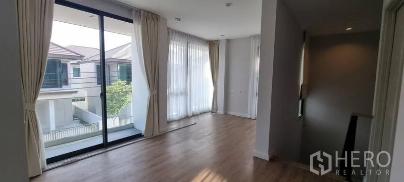 Detached House for rent in Saphan Sung, Bangkok - Upstairs family area with balcony access, wood flooring, and full-height curtains.