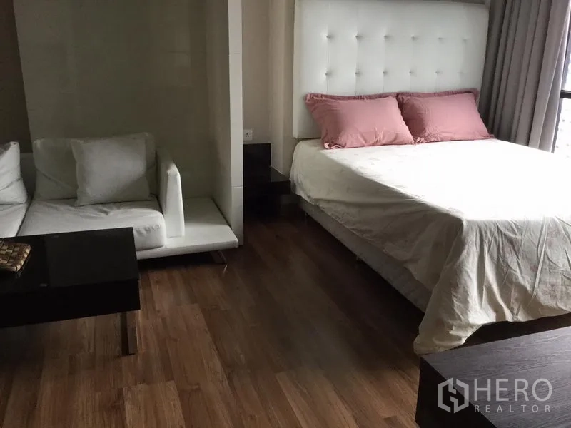 คอนโด ให้เช่าในHuai Khwang, Bangkok - ห้องสตูดิโอพร้อมเตียงหัวเตียงบุหนัง มุมโซฟา และพื้นไม้ใกล้หน้าต่างบานใหญ่