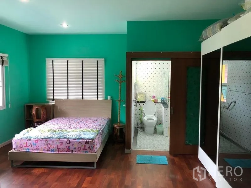 Detached House for sale in Wang Thonglang, Bangkok - Spacious bedroom with teal walls, wood floors and an ensuite bathroom.