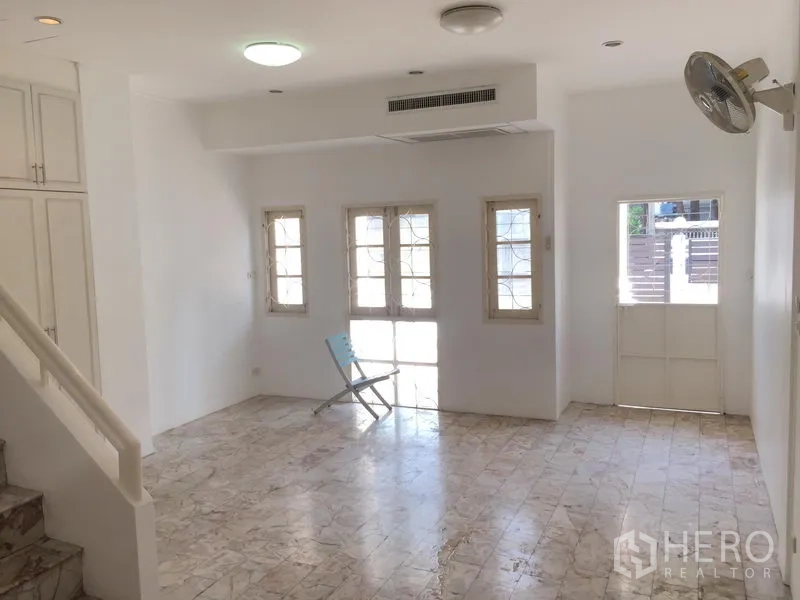 Townhouse for rent in Chatuchak, Bangkok - Open-plan lounge with multiple French windows, wall fan and a door to the front courtyard.