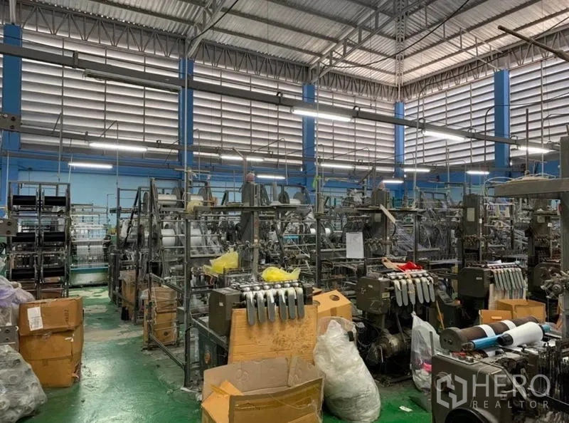 Warehouse for sale in Mueang Samut Sakhon, Samut Sakhon - Wide industrial floor filled with machinery beneath louvered wall vents and steel trusses.