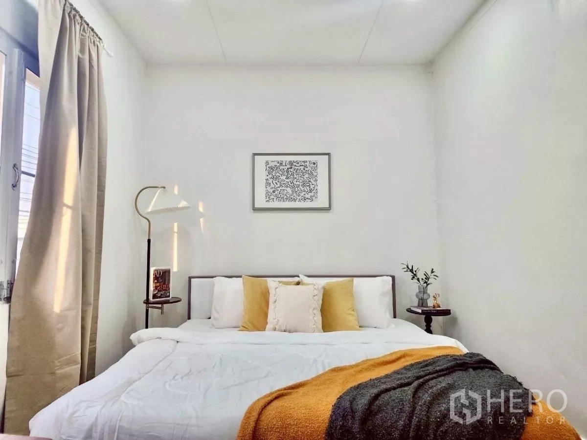 独立式住宅 出租在Chatuchak, Bangkok - 温馨卧室，柔和灯光，白色床品与芥末黄披毯。