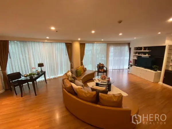 Apartment for rent in Watthana, Bangkok - Spacious living room with a curved sofa, floor-to-ceiling windows and a built-in TV wall.