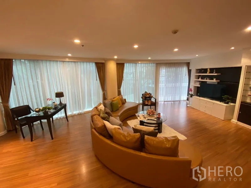 Apartment for rent in Watthana, Bangkok - Spacious living room with a curved sofa, floor-to-ceiling windows and a built-in TV wall.