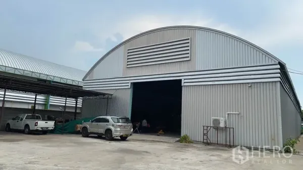 Warehouse for rent in Lak Si, Bangkok - Front view of a large arched‑roof steel warehouse with a wide sliding entrance and concrete yard in Lak Si, Bangkok.