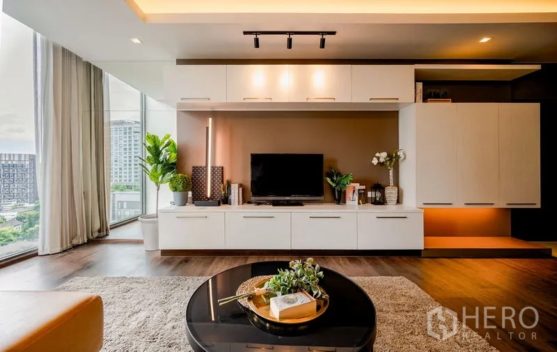 Condominium for sale in Khlong Toei, Bangkok - Entertainment wall with TV on low cabinets, plants, and floor-to-ceiling windows showing a city view.