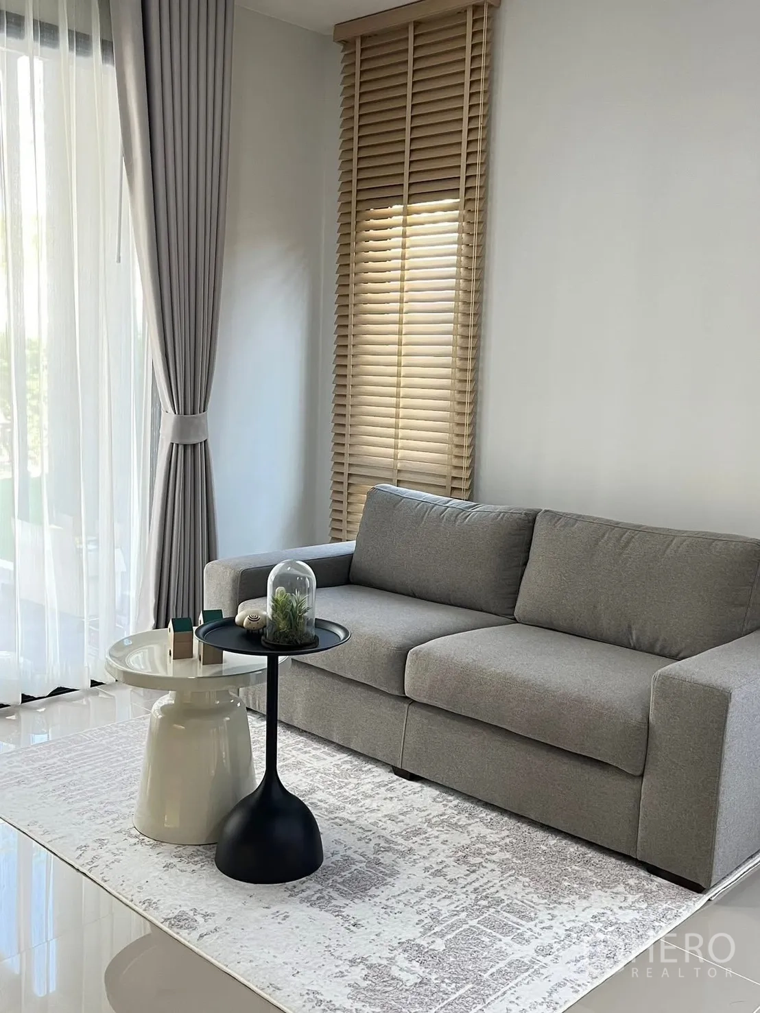 Townhouse for rent in Bang Phli, Samut Prakan - Living area with gray sofa, side tables, large windows with curtains, and blinds.