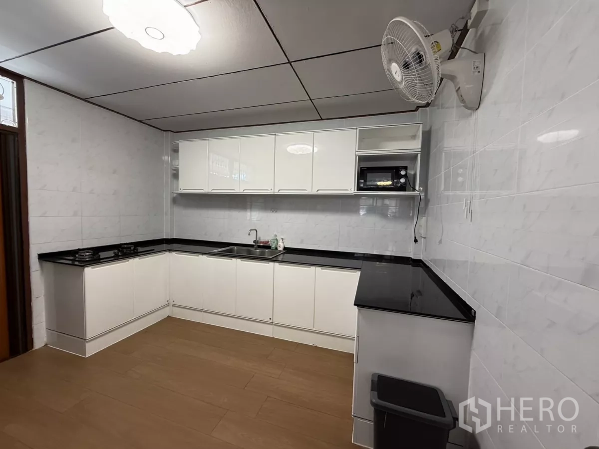 Detached House for rent in Phra Khanong, Bangkok - L-shaped kitchen with white cabinets, black countertops and sink.