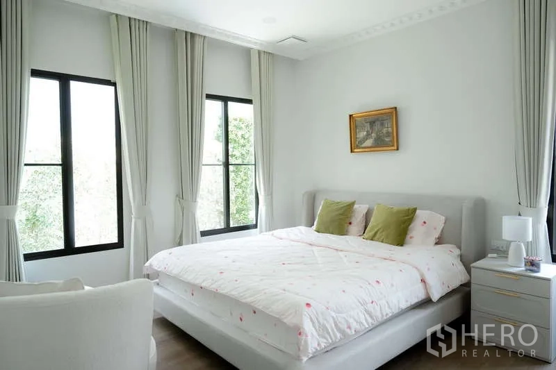 Detached House for rent or sale in Saphan Sung, Bangkok - Sunlit bedroom with corner windows, light curtains and a queen-sized bed.