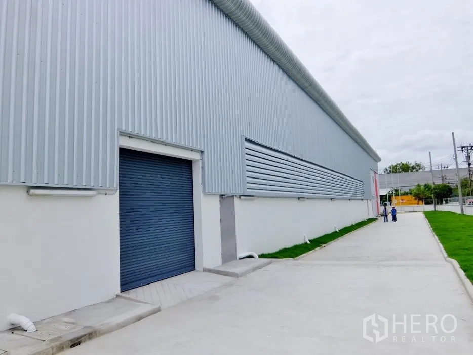 Factory for rent in Bang Sao Thong, Samut Prakan - Metal-clad factory exterior with roller shutter door, private side road and green verge.