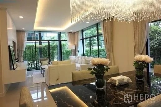 Detached House for rent or sale in Prawet, Bangkok - Open-plan living and dining room with chandelier, floor-to-ceiling windows, and garden views.
