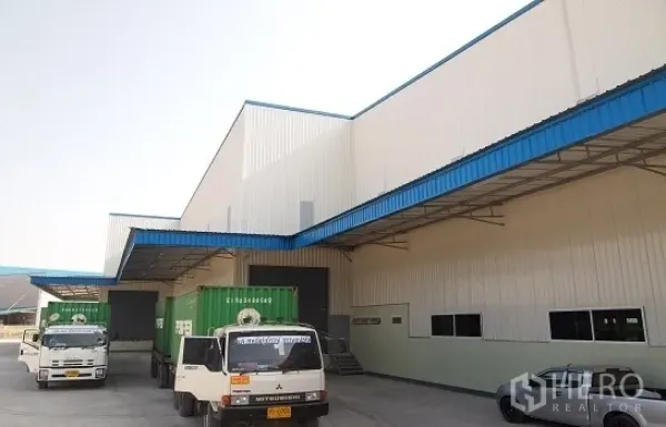 โรงงาน ให้เช่าในSi Racha, Chon Buri - ลานโหลดสินค้ามีหลังคาพร้อมรถบรรทุกตู้คอนเทนเนอร์ หน้าโรงงานสีขาวคาดสีน้ำเงินในศรีราชา