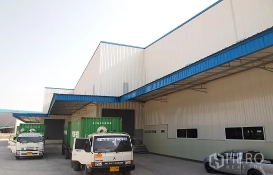 โรงงาน ให้เช่าในSi Racha, Chon Buri - ลานโหลดสินค้ามีหลังคาพร้อมรถบรรทุกตู้คอนเทนเนอร์ หน้าโรงงานสีขาวคาดสีน้ำเงินในศรีราชา