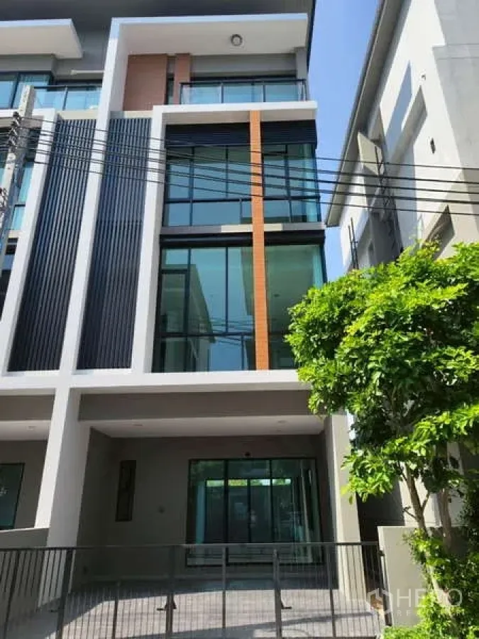 带办公室的家 出租在Bueng Kum, Bangkok - 现代多层联排式商住办公楼外立面，大面积落地玻璃与竖向百叶，前方带围栏车位。