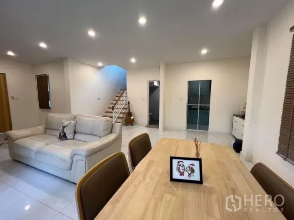 Detached House for sale in Bang Kruai, Nonthaburi - Open‑plan living and dining room with sofa, wooden table, glossy tile floor and staircase.