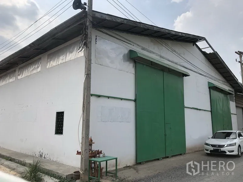 货栈 出租或出售在Khlong Luang, Pathum Thani - 仓库外立面，白色墙体与大型绿色推拉门，金属屋顶，位于空銮巴吞他尼的路边。