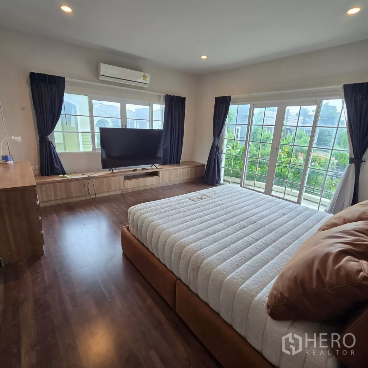 Detached House for rent in Mueang Pathum Thani, Pathum Thani - Bright master bedroom with balcony doors, TV console and king-size bed.