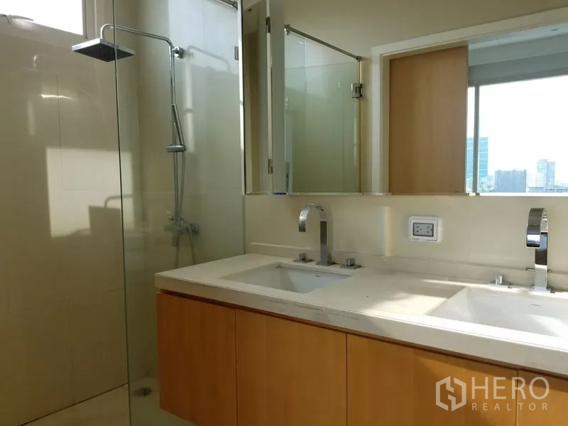 Condominium for rent in Chatuchak, Bangkok - Bright bathroom with double sinks, a large mirror and a glass‑enclosed shower.