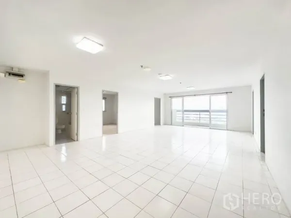 Condominium for sale in Bang Na, Bangkok - Spacious white-tiled living room with sliding glass doors opening to a balcony and city view.