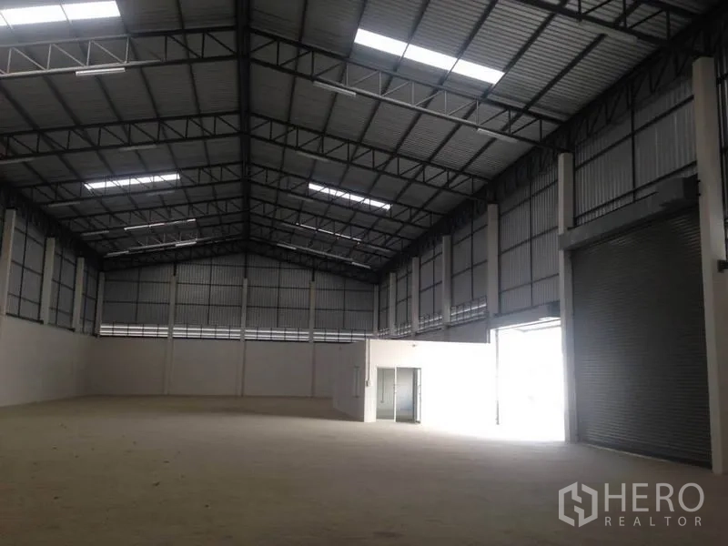 货栈 出租在Bang Bua Thong, Nonthaburi - 仓库内部空间高挑，钢桁架屋顶与天窗，配高卷闸门