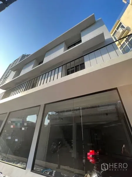 Shophouse for rent in Khlong Toei, Bangkok - Low-angle view of a newly renovated multi‑storey shophouse with modern balconies and large windows under a clear sky.
