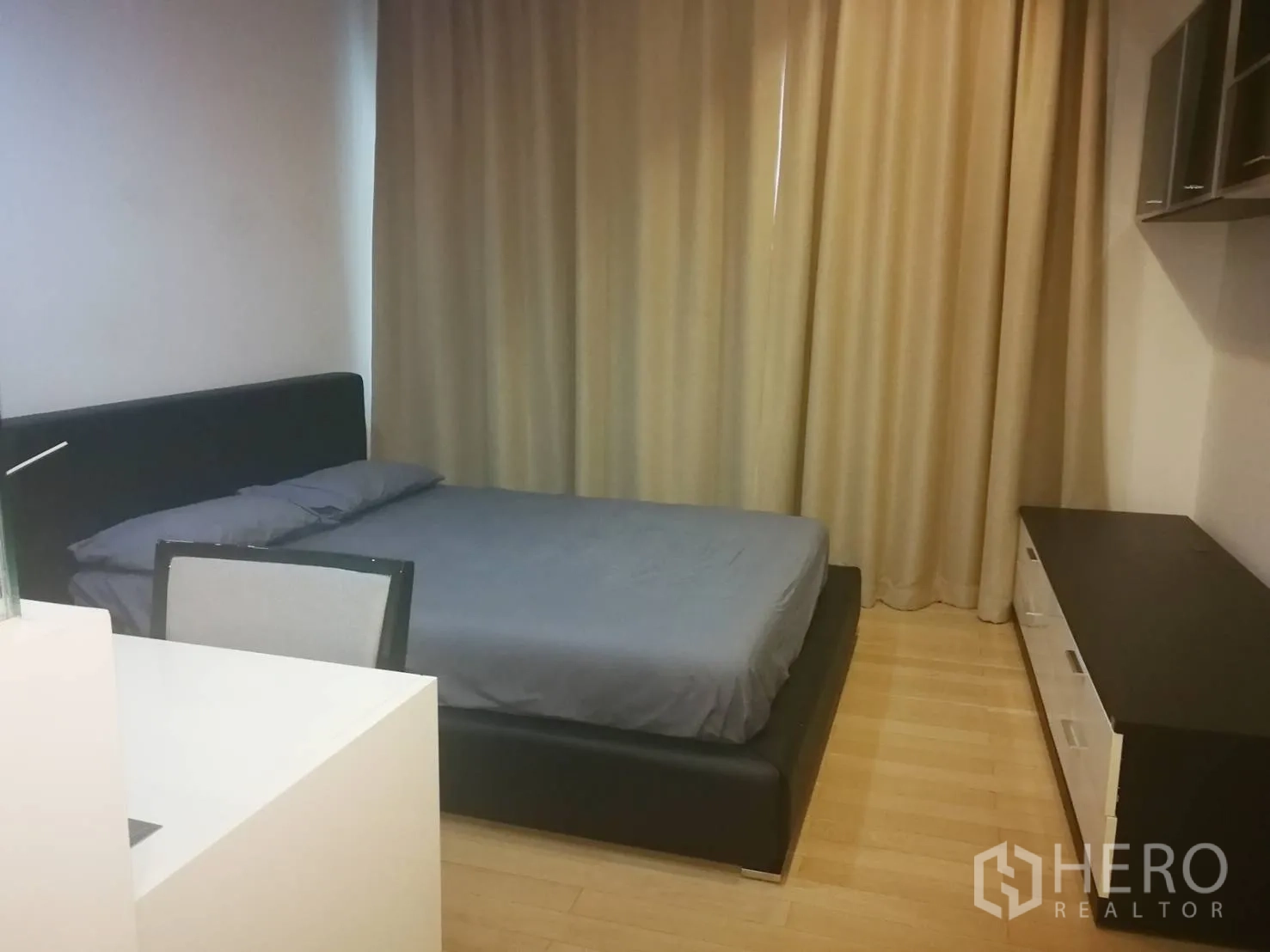 Condominium for rent in Khlong Toei, Bangkok - Bedroom with double bed, work desk, storage cabinet and blackout curtains on wood floors.