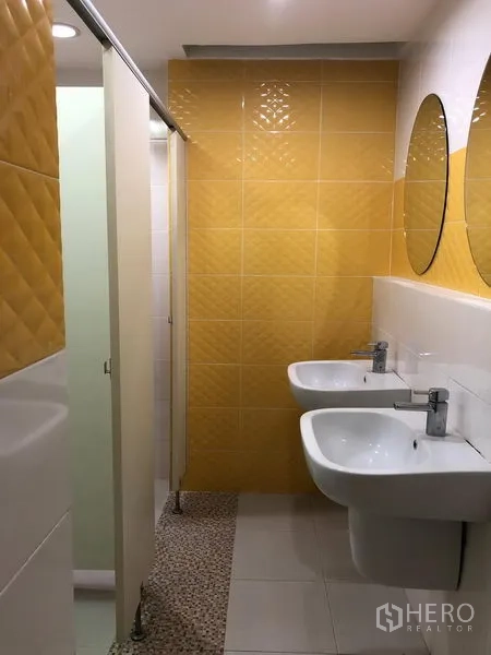 Office Space for rent in Bang Na, Bangkok - Modern restroom with yellow wall tiles, twin sinks and private cubicles.