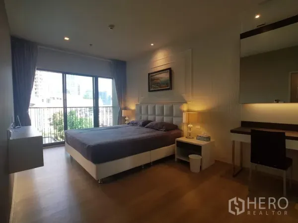 Condominium for rent in Bangkok - Bright master bedroom with upholstered headboard, bedside lamps and balcony access through floor-to-ceiling glass with city view.