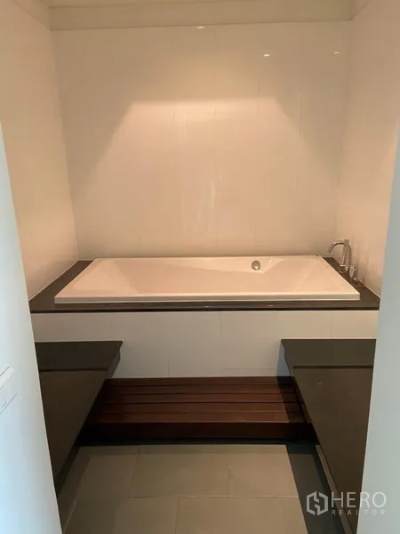Condominium for rent in Khlong Toei, Bangkok - Bathroom featuring a recessed soaking bathtub with benches on both sides.