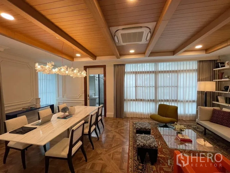 Detached House for rent or sale in Saphan Sung, Bangkok - Warm dining and lounge space with wood-beam ceiling, long marble table and large curtained windows.