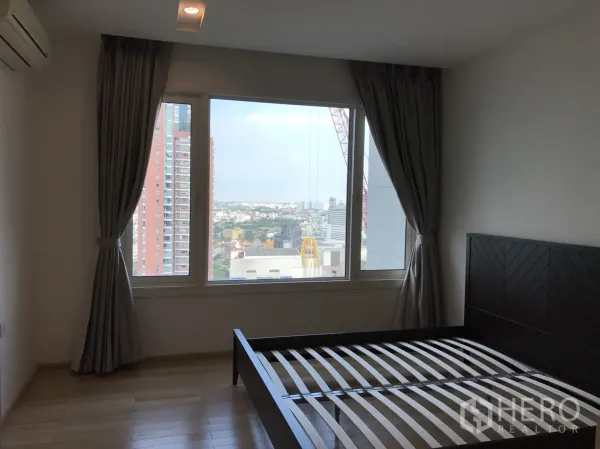 Condominium for rent in Khlong Toei, Bangkok - Bedroom with large window, wooden flooring and city skyline outlook in a high‑rise condo.