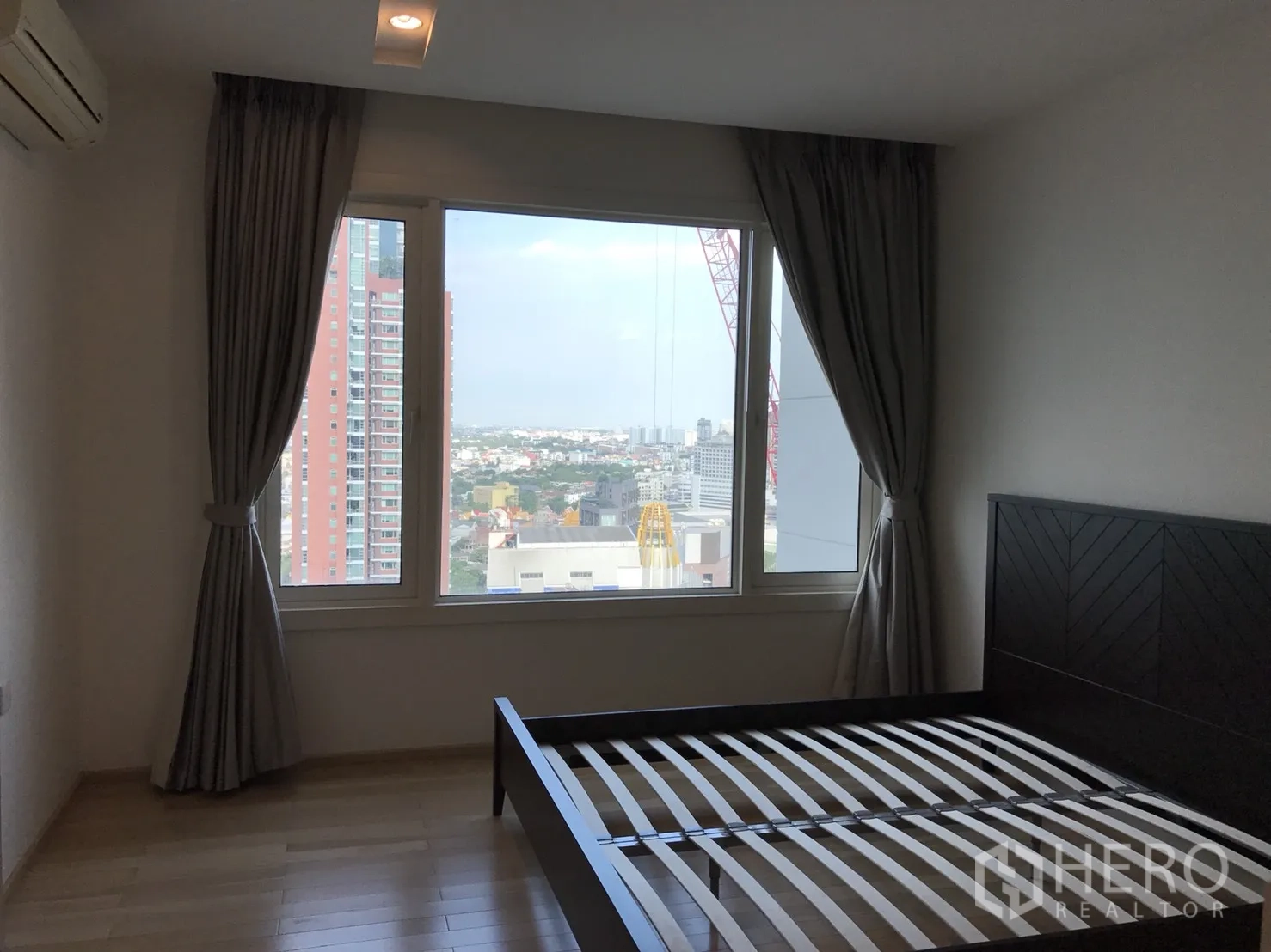Condominium for rent in Khlong Toei, Bangkok - Bedroom with large window, wooden flooring and city skyline outlook in a high‑rise condo.