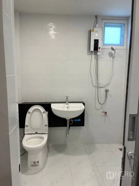 Detached House for rent in Samut Prakan - Bright tiled bathroom with toilet, sink, and wall‑mounted shower heater.