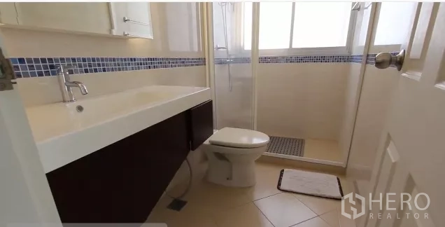 公寓 出租在Watthana, Bangkok - 浴室配玻璃淋浴房、洗手台和马桶，蓝色马赛克点缀。
