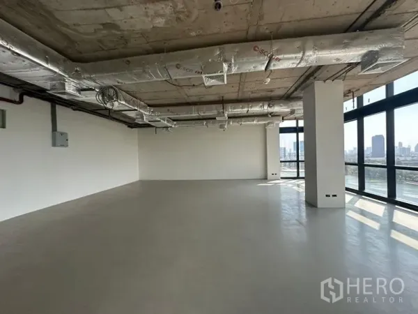 办公空间 出租在Watthana, Bangkok - 室内空间宽阔，抛光地坪、白色墙面、暴露式空调管道，转角窗框出城市景。