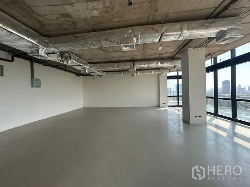 办公空间 出租在Watthana, Bangkok - 室内空间宽阔，抛光地坪、白色墙面、暴露式空调管道，转角窗框出城市景。