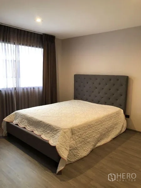 Townhouse for rent in Lat Phrao, Bangkok - Cozy second bedroom with tufted headboard, large window, curtains and wood floors.