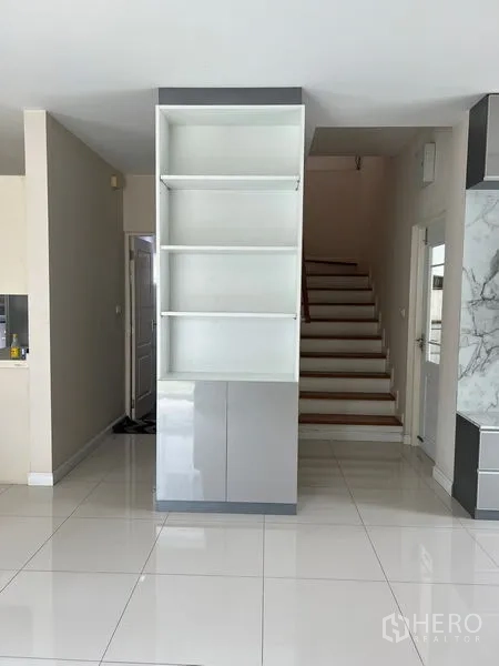 Detached House for rent in Bang Kapi, Bangkok - Hallway with glossy tile floors, built-in shelving, and staircase to the upper level.