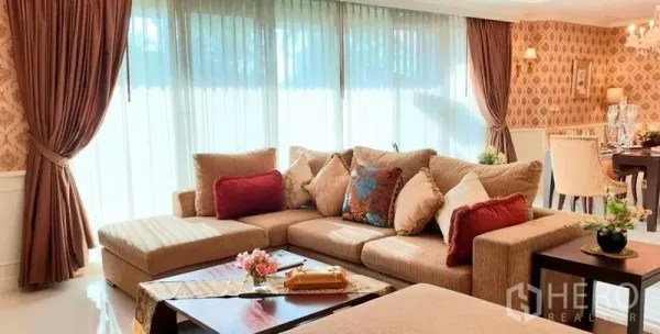 Apartment for rent in Watthana, Bangkok - Bright living room with L‑shaped sofa, sheer floor‑to‑ceiling windows and patterned wallpaper.